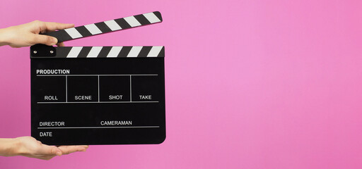 Two hands are holding a black clapper board or movie slate on pink background.