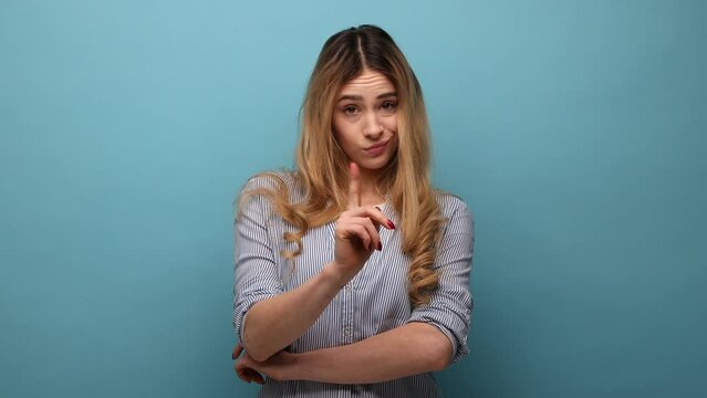 Bossy caution. Portrait of serious angry woman pointing finger, showing warning gesture at camera, alarming to be careful, wearing striped shirt. Indoor studio shot isolated on blue background.