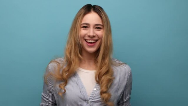 Portrait of funny disobedient young adult woman demonstrating tongue, behaving naughty unruly, childish mood, wearing striped shirt. Indoor studio shot isolated on blue background.