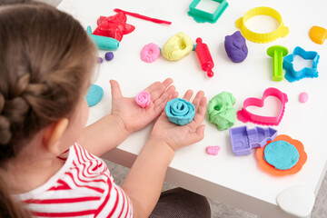 baby girl sculpts rose flowers from plasticine, play dough, playdough, mass for modeling, set for creativity