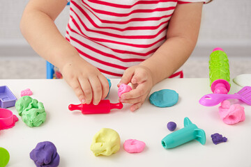Obraz na płótnie Canvas children's hands sculpt plasticine figures with rolling pin on white table, games with play dough, playdough, mass for modeling, set for creativity
