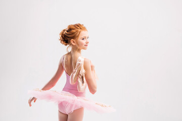Portrait of a little tender red-haired girl in a pink tutu with pointe shoes, dreaming of becoming...