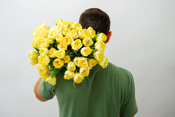 portrait of man from back with bouquet of yellow tulips on his shoulder