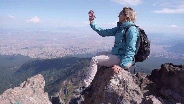 woman in blue jacket making photos with her smartphone in the mountain