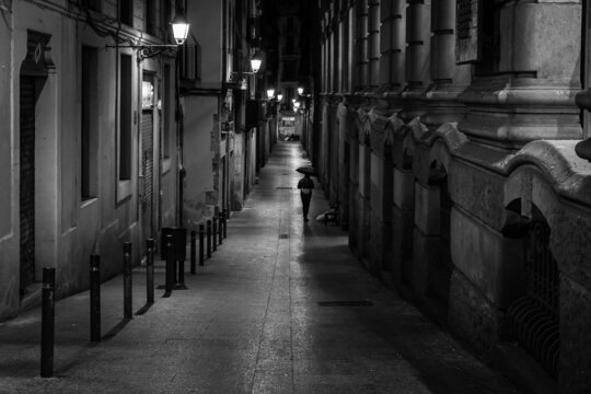 Fototapeta Man with umbrella at night in an alley in the Gothic Quarter of Barcelona illuminated with lanterns. Black and white photo