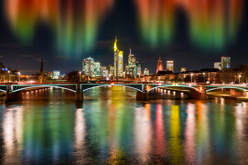 Fototapeta premium Die Skyline von Frankfurt am Main am Abend mit Nordlichtern und Fluss im Vordergrund