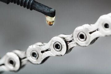 Greasing a bicycle chain with a drop of golden oil close-up on a gray background