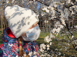 Obraz premium a girl in a hat and a medical mask sniffs a flowering branch in the park