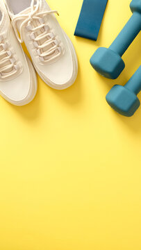 Feminine sport shoes, dumbbells, fitness tape on yellow background top view. Sport blog vertical banner design