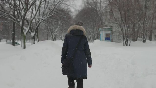 Heavy snowfall in the city. A woman walks along a snowy winter alley.