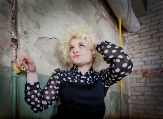 Curly girl - blonde in a blouse with polka dots like a clown in an old, ruined interior