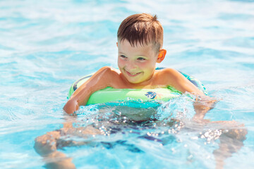 Fototapeta na wymiar Funny happy child boy in swiming pool on inflatable rubber circle ring. Kid playing in pool. Summer holidays and vacation concept