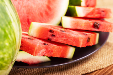 Fresh red watermelon pieces on a black plate on a wooden table. Sweet and juicy watermelon