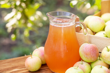 Apples, box of apples and pitcher of fresh apple juice on wooden table with garden background. Harvest of apples. Juice production
