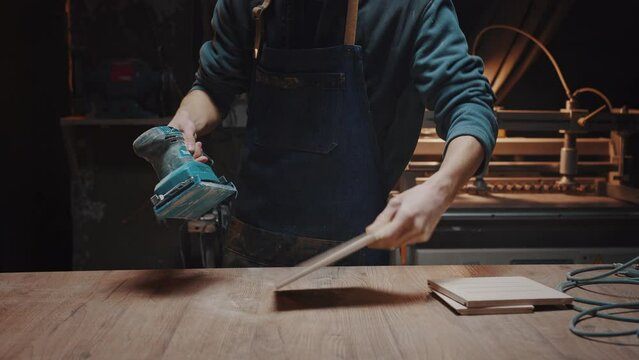 Close-up of a woodworker's hand sanding wood details with a grinder in his workshop. Cinematic effect