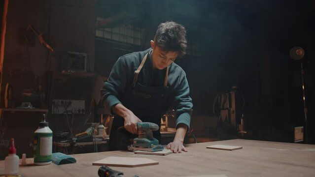 Carpenter and his small family business. Young man works in his workshop, polishing wooden parts and blanks. Handmade wooden products