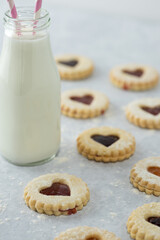 Heart shaped Valentines day or holiday homemade cookies with different jams  and jar of milk in the background from a vertical elevated front angle on a marble table.