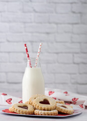 Homemade jam cookies and jar of milk on a marble table with subway tile white background.