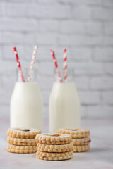 Homemade jam cookies and jar of milk on a marble table with subway tile white background.