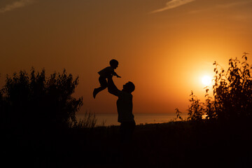Fototapeta na wymiar Silhouette of a man and a child against the sunset.Dad raises his son 