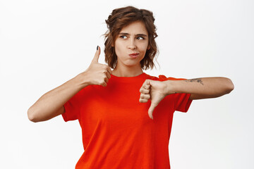 Portrait of brunette female model showing thumbs up and thumbs down, like or dislike gesture,...