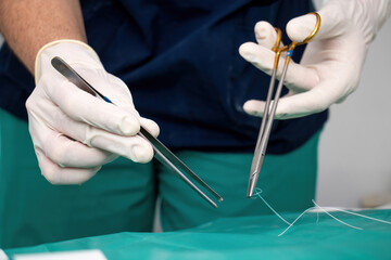 Doctor surgeon with disposable glove on hand make suture holding forceps, scissor over green fabric