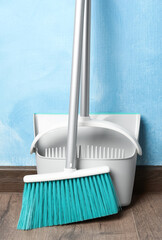 Plastic broom with dustpan near light blue wall indoors