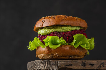 Vegan burger with beetroot, avocado sauce and lettuce salad on black background. Healthy vegetarian...