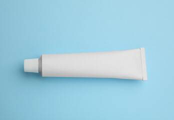 Blank white tube of ointment on light blue background, top view. Space for text