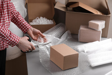 Woman cutting bubble wrap at table in warehouse, closeup