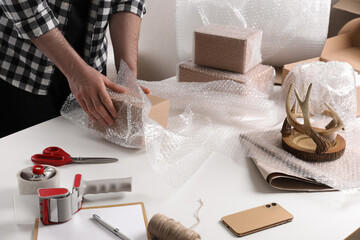 Man covering box with bubble wrap at table in warehouse, closeup