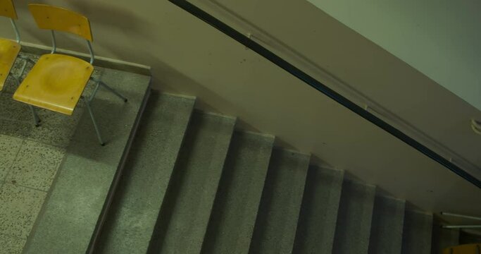 In an abandoned school at the stairway, a pan from two chairs to a bunch of laying down chairs, the school is from the 70&rsquo;s
