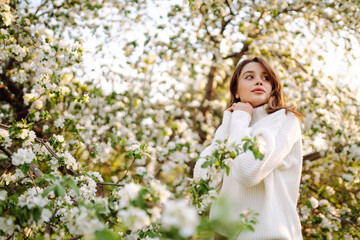 Fototapeta premium Young woman enjoying scent in blooming spring garden. The concept of relax, travel, freedom and spring vacation. Fashion style