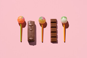 Colorful Set of Lollipops and chocolate. pattern made with caramel on a stick and chocolate on bright pink background.  creative pattern.  lot of lollipops chupa chups.