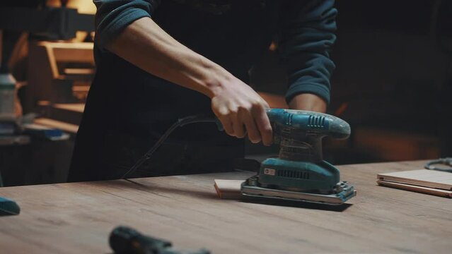Close up of a carpenters hands with a grinder. A young apprentice guy works in a carpentry workshop, polishing parts for handmade birdhouses