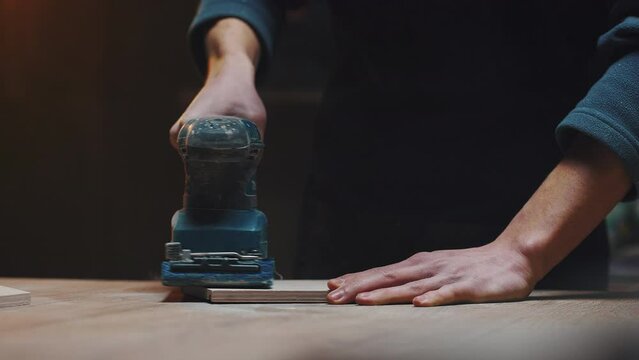 Manufacture of wooden houses for animals. Man's hands with a grinder. Unidentifiable carpenter sanding wooden blanks in his workshop