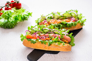 Ready to eat hot dogs with sausage, cucumber, tomato and herbs on a slate on the table. Fast food for a snack.