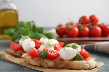 Fototapeta na wymiar Delicious sandwiches with mozzarella, fresh tomatoes and basil on blue wooden table. Space for text
