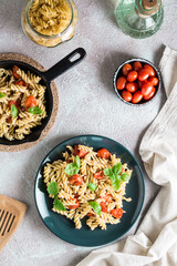 A plate of pasta with tomatoes and basil on a plate and cooking ingredients on the table. Mediterranean cuisine. Vertical and top view