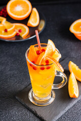 Orange cranberry fizzy cocktail in a glass and fruits and berries nearby on a slate on a dark background. Homemade mocktail. Vertical view