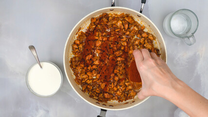 Woman adds paprika into a frying pan with chopped chicken fillet. Cooking Hungarian paprikash, or sour cream chicken paprika. Step by step recipe