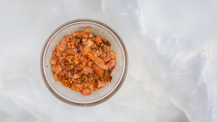 Chopped chicken fillet marinated with garlic, seasoning, paprika, and soy sauce close up in a glass bowl on marble background