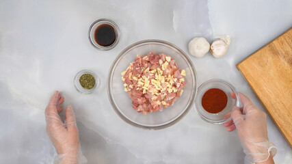 Chopped chicken fillet with chopped garlic and some ingredients for marinade close up on kitchen table. Sour cream chicken paprika recipe, step by step cooking process, part of series