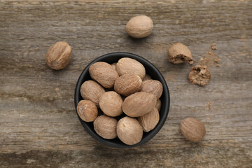 Bowl with nutmeg seeds on wooden table, flat lay