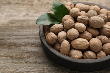 Plate with nutmeg seeds and green leaves on wooden table, closeup. Space for text