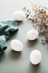 White chicken eggs, linen napkin and eucalyptus branch on a green background. Eco friendly happy easter. Vertical view