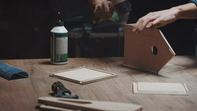 Man assembles a wooden house from blanks. Close-up of a craftsman's hand with a wooden hammer and blanks. Glue a pet house