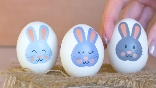 Easter eggs with a bunny pattern. Drawing with paints on a white egg. Woman's hand arranges pascal eggs