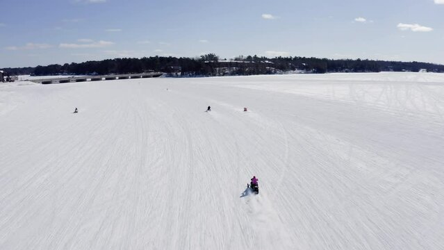 Aerial above passing snowmobiles on snowy frozen lake in northern Wisconsin. Snowmobiling on winter sunny day