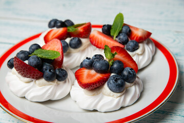Four cakes Anna Pavlova with blueberries and strawberries with a mint leaf on a beautiful plate. Home confectionery. Old retro white and blue table.
